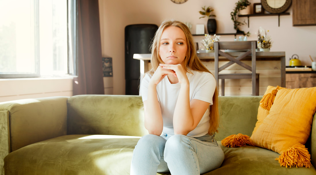 This young woman sitting on her couch and staring into space has no energy to declutter. 